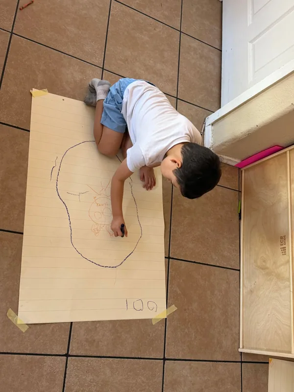 A boy drawing on a big sheet of paper on the floor